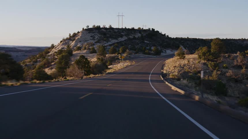 A point-of-view shot driving down a winding road through a rocky, desert landscape during golden hour