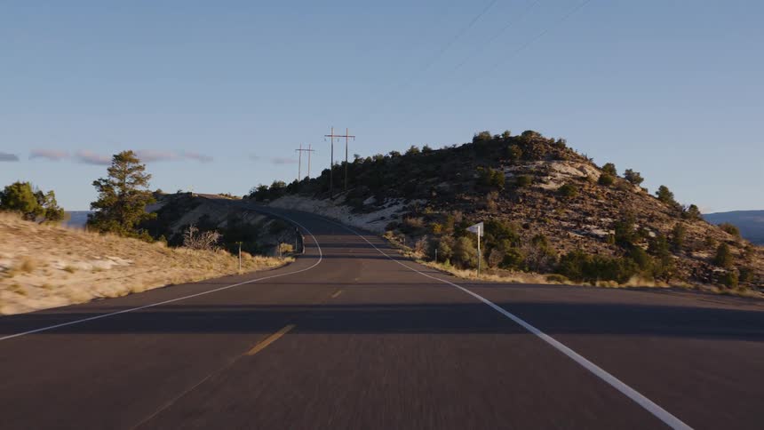A point-of-view shot driving along a winding scenic highway through a hilly desert landscape during the golden hour