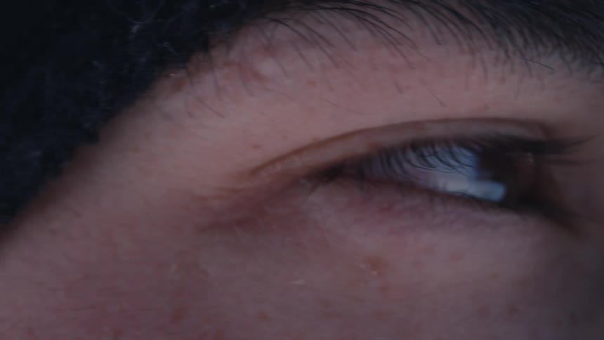 An intimate macro view captures the detailed texture of a person's skin and eyelashes as their eye scans the surroundings and slowly closes