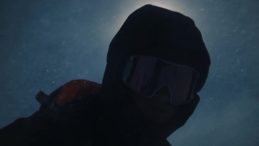 Dramatic slow-motion reveal of a mysterious skier in a balaclava and goggles standing silhouetted against the sun in a blizzard
