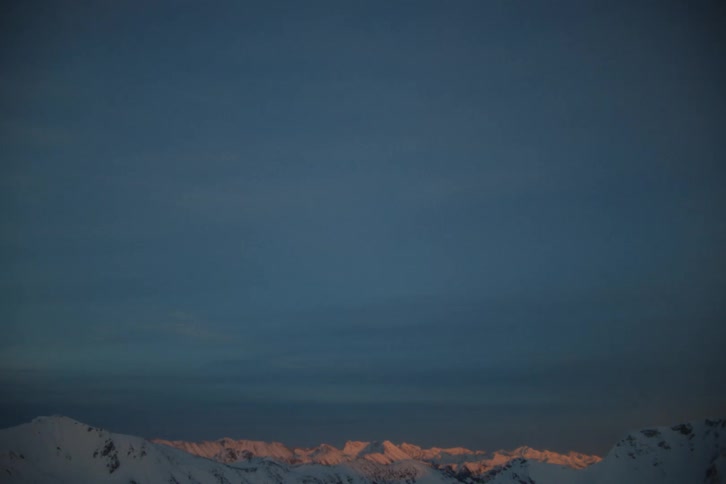The last light of sunset kisses the peaks of a distant snow-covered mountain range under a deep blue sky