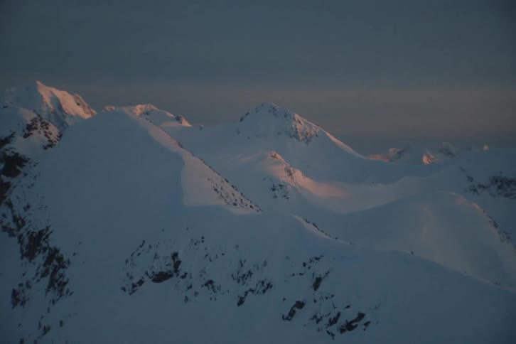 A slow zoom into a serene, snow-covered mountain range as the last light of sunset illuminates the distant peaks