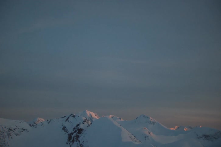 A slow pan reveals a vast, snow-covered mountain range as the sunrise casts a warm glow on the peaks