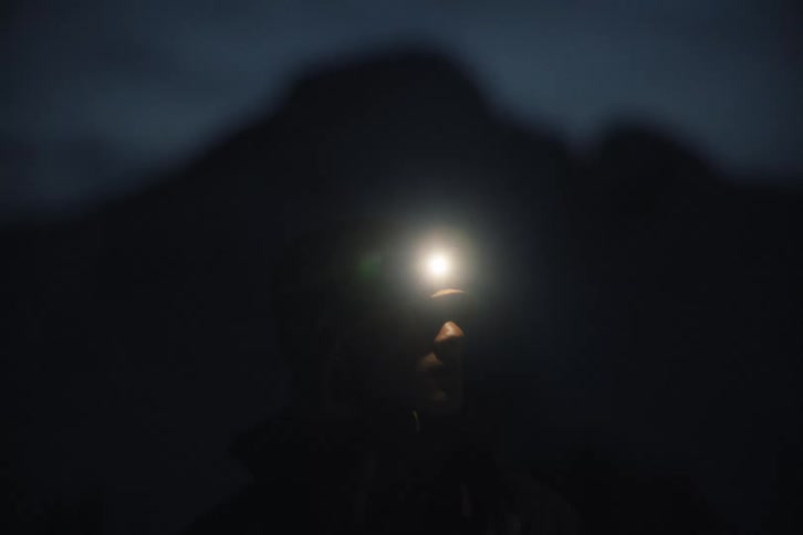 Close up on a hiker turning on their headlamp at night in the mountains, creating a bright lens flare