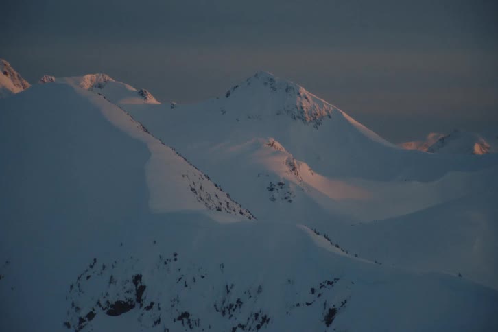 A slow zoom reveals majestic, snow-covered mountain peaks catching the warm, golden light of sunrise