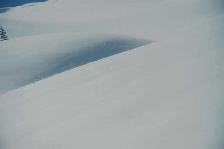 Wind blows fine powder snow across a vast and pristine, sunlit snowscape