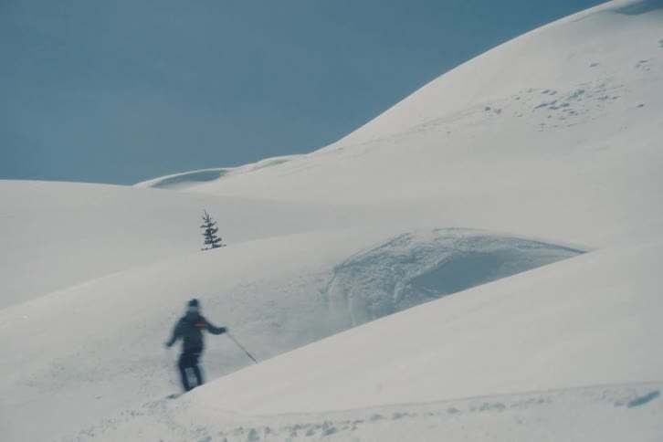 Slow motion wide shot of a professional skier carving through fresh powder on a vast, minimalist, snow-covered mountain