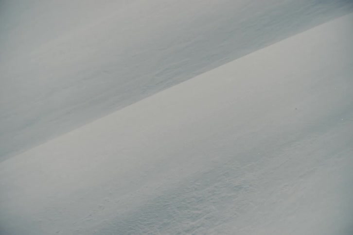 Abstract close-up shot of a snowdrift with fine snow particles blowing across the surface during a winter storm