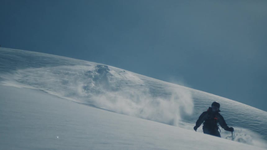 In breathtaking slow motion, a skier emerges over a snowy ridge and glides through untouched powder before unleashing a massive spray of snow