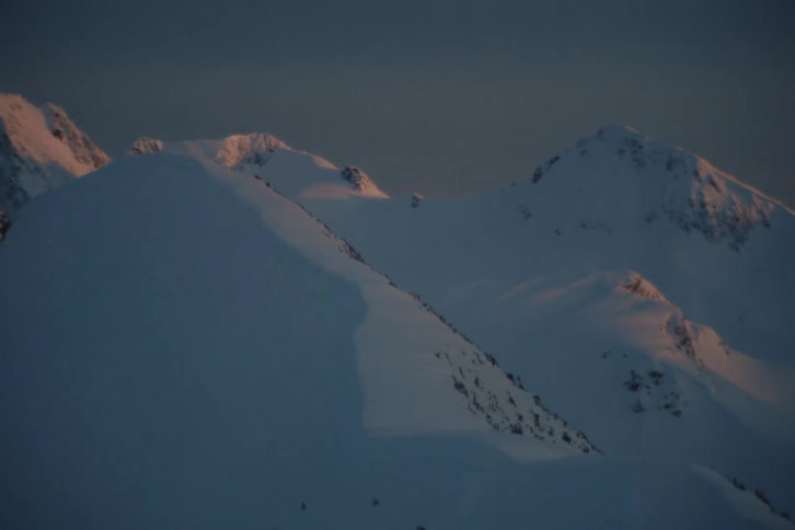 A slow pan across a vast, snow-covered mountain range as the golden light of sunrise illuminates the distant peaks