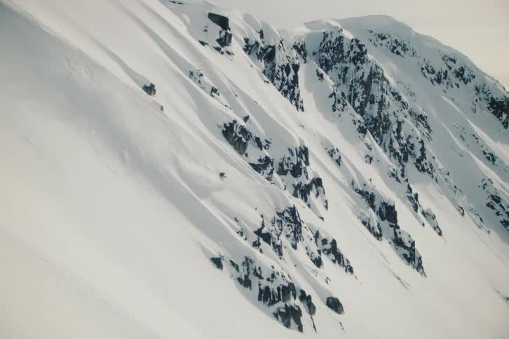 An extreme skier carves through fresh powder down a vast and steep mountain face