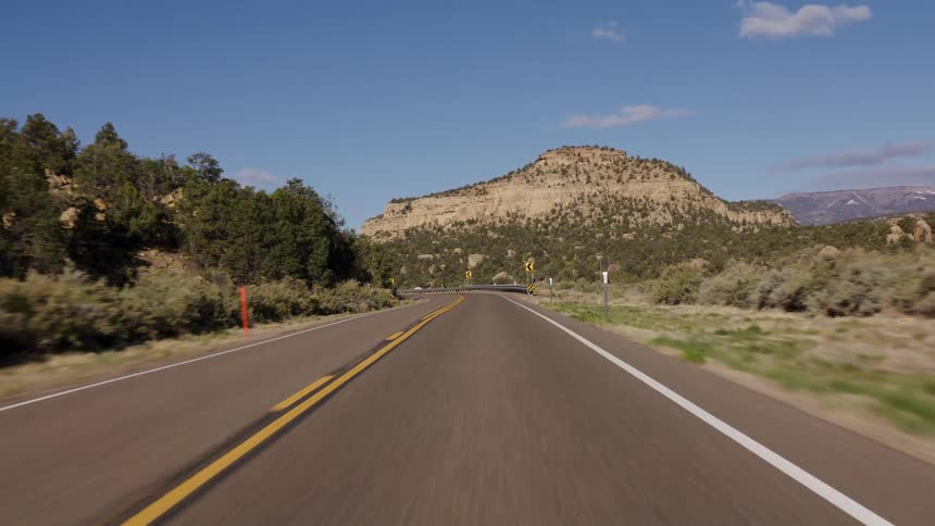 A first-person perspective of a scenic drive on a winding desert road through a canyon on a sunny day