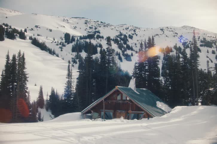 Picturesque view of a mountain cabin half-buried in fresh powder snow on a sunny winter day