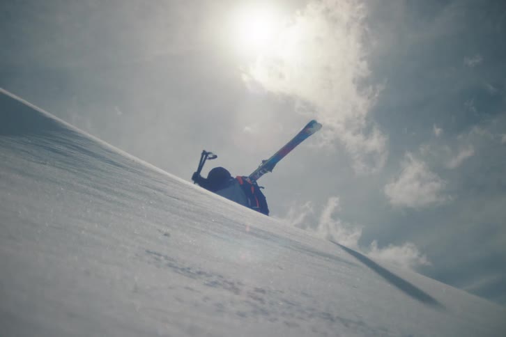 A determined ski mountaineer climbs a steep, snowy slope with an ice axe as the sun shines brightly overhead