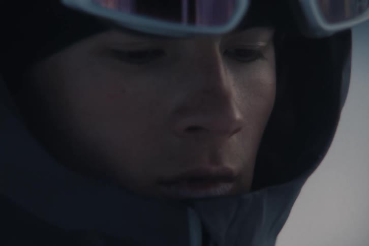A pensive skier dressed in warm gear stands on a snowy mountain, captured in a dramatic slow-motion close-up