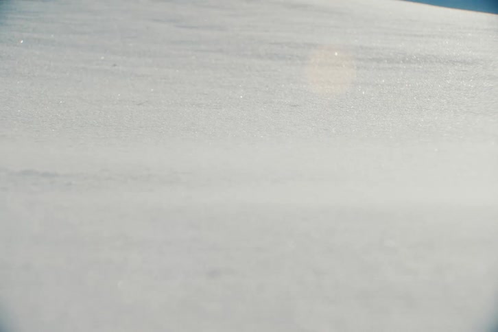 A close-up shot of glistening fresh snow as the wind gently blows it across the ground on a sunny winter day