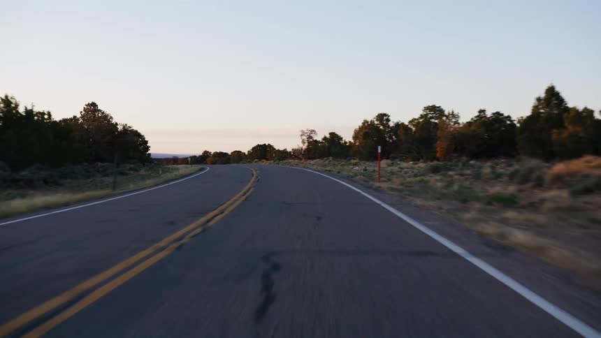 POV driving along a winding, empty desert highway through scrubland at golden hour