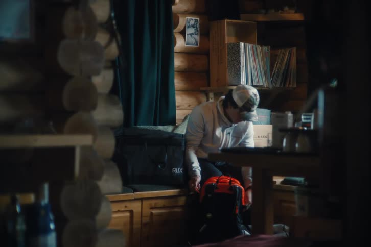 Inside a cozy log cabin, a man carefully packs his backpack with winter gear for an upcoming adventure