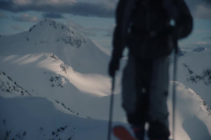 A backcountry skier walks out of frame, leaving a stunning vista of a vast, snow-covered mountain range