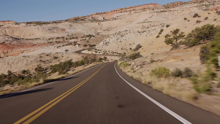 Point-of-view shot driving down a scenic, winding asphalt road through a beautiful desert canyon landscape
