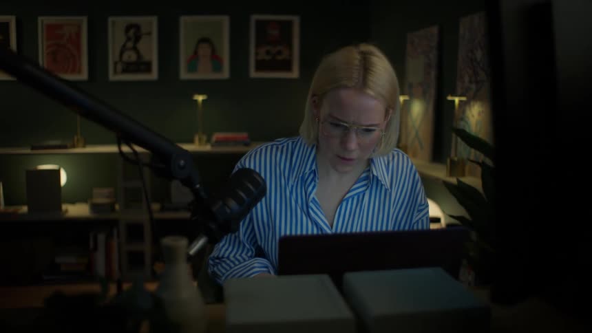 A focused woman working late at her desk in a dark room becomes visibly concerned by what she sees on her computer
