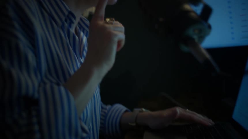 A female podcaster passionately discusses financial markets while gesturing and analyzing charts on her laptop late at night