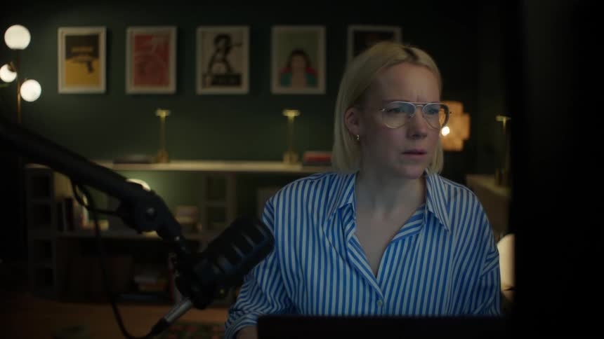 A focused female graphic designer with glasses works late at night in her stylish home office studio on her computer
