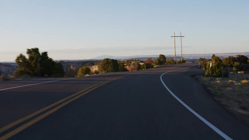 A smooth point-of-view drive along a scenic and winding desert highway during a beautiful golden hour sunrise