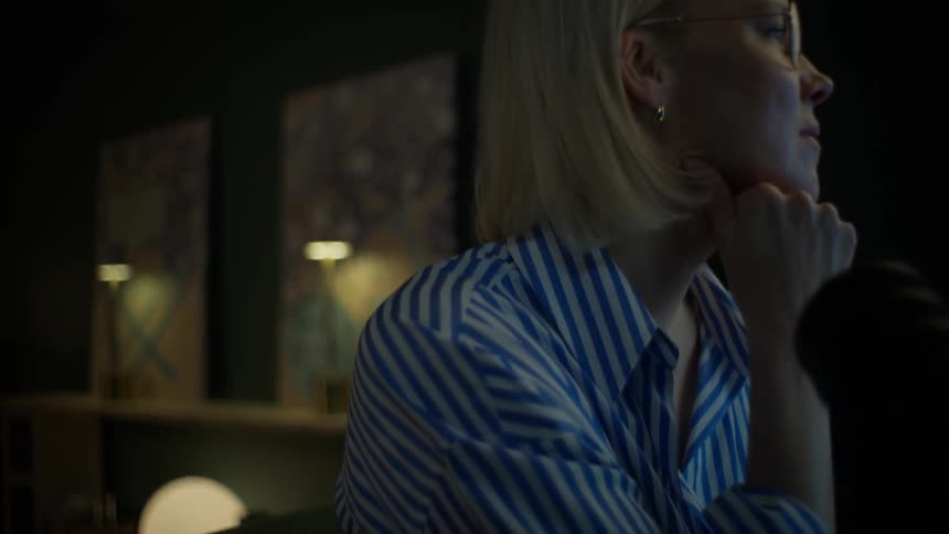 A focused businesswoman smiles contentedly while working in slow motion on her laptop late at night in her cozy home office
