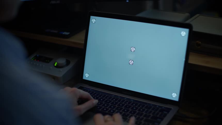 Over-the-shoulder shot of a person typing on a laptop with a chroma key screen and tracking markers in a dark room