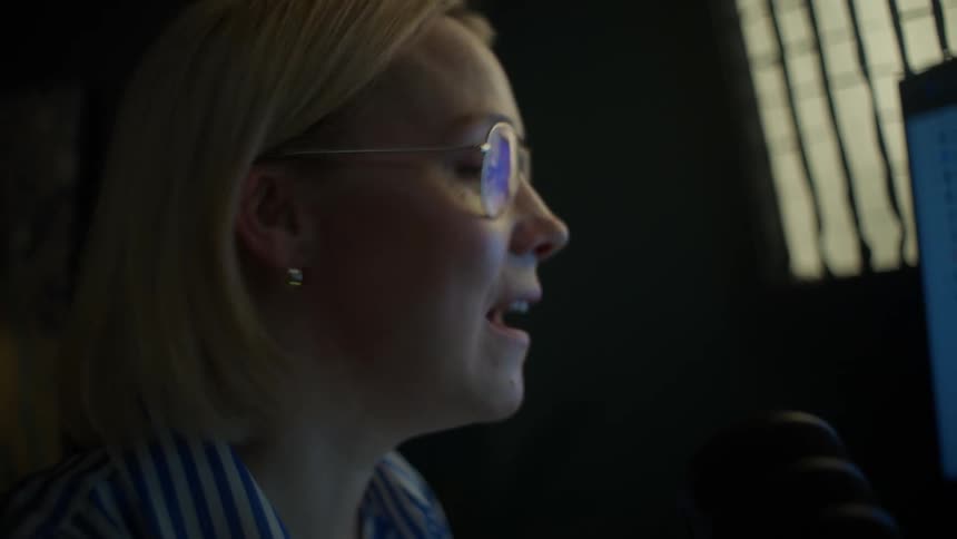 A female financial analyst with glasses passionately discusses stock market data while recording a podcast in her professional home studio at night