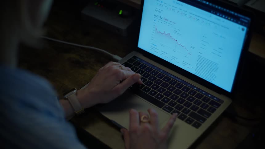 An investor monitors the declining stock market on a laptop in a dimly lit room