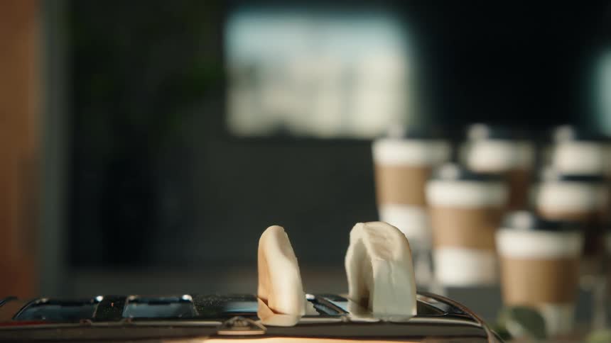 A slow-motion close-up of perfectly toasted and burnt bread popping out of a toaster in a kitchen