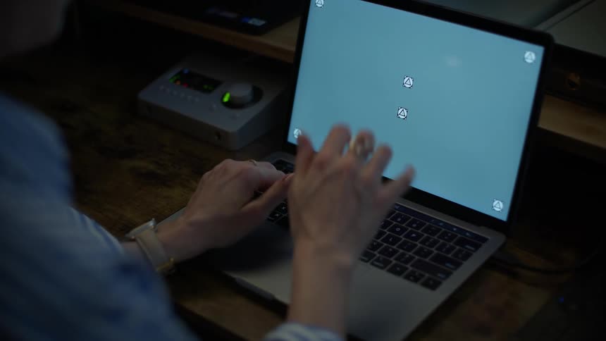 An over-the-shoulder shot of a woman typing on a laptop with a screen ready for compositing in a dimly lit room