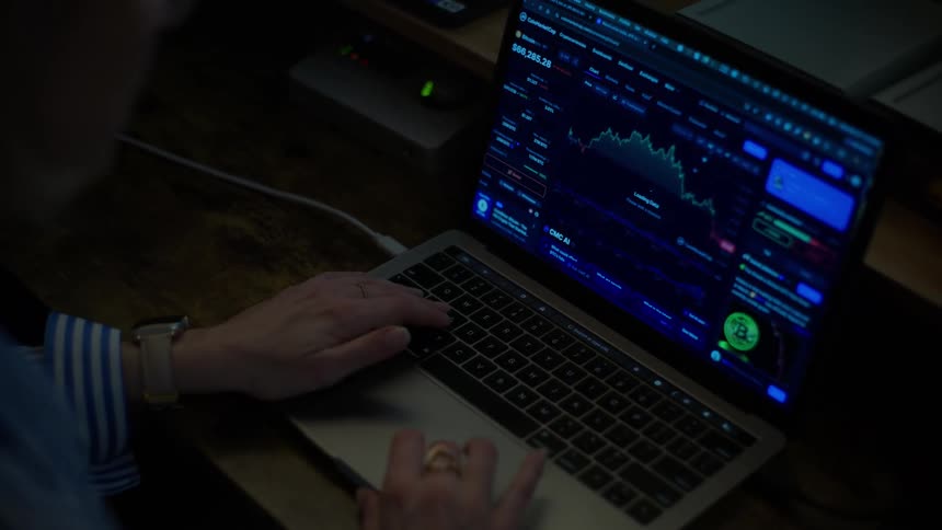 An over-the-shoulder view shows a financial trader analyzing a crashing cryptocurrency market on a laptop in a dark office