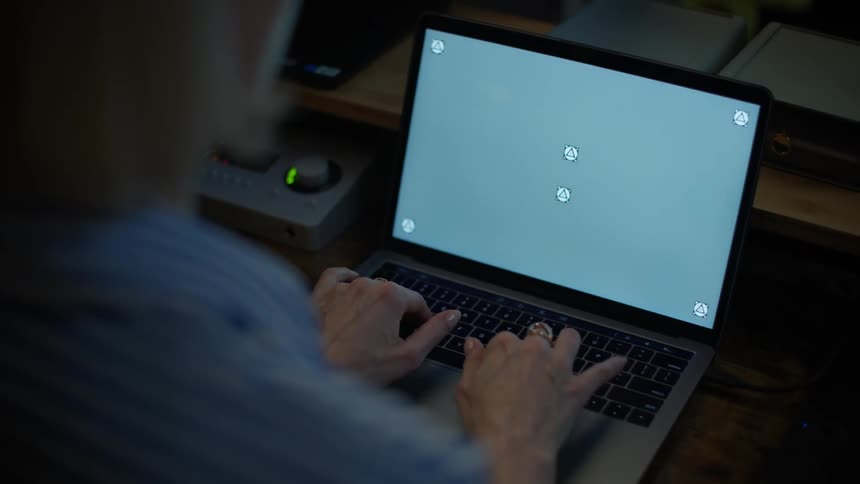An over-the-shoulder view of a woman typing on a laptop with a track-marked screen for compositing in a dimly lit room