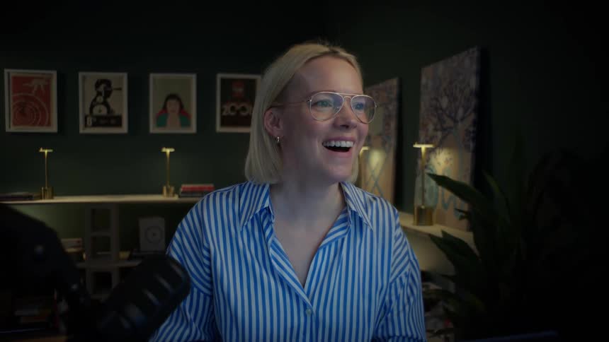 A creative professional woman working late in her home studio is surprised and laughs while looking at her computer monitor