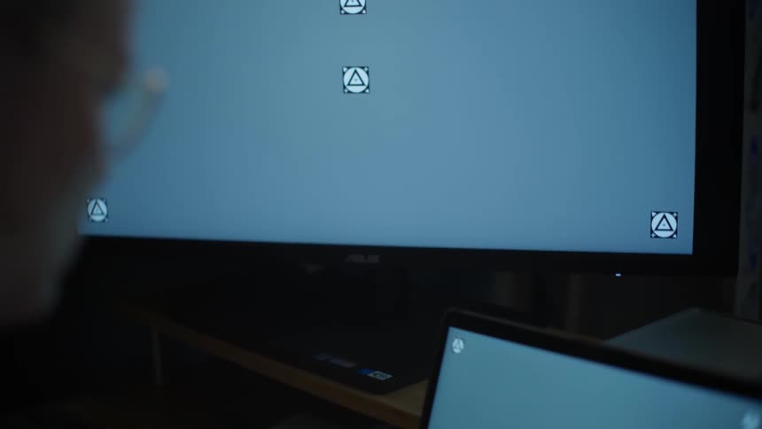 Over-the-shoulder shot slowly revealing a person's dual-monitor setup with tracking markers for screen replacement in a dark office