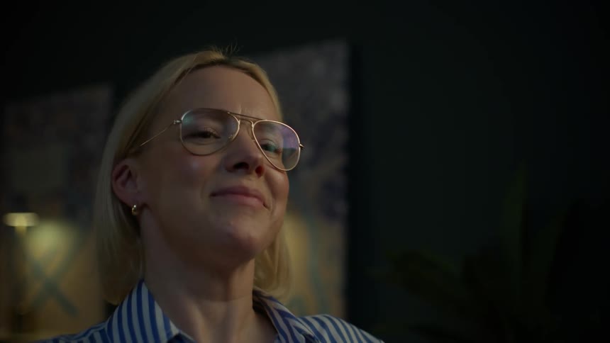 A woman in glasses finishes her work late at night, closes her laptop, and smiles with satisfaction
