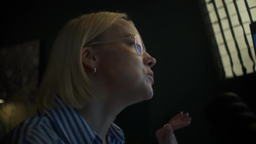 A female podcaster gestures and speaks passionately into a microphone while streaming in a dark room at night