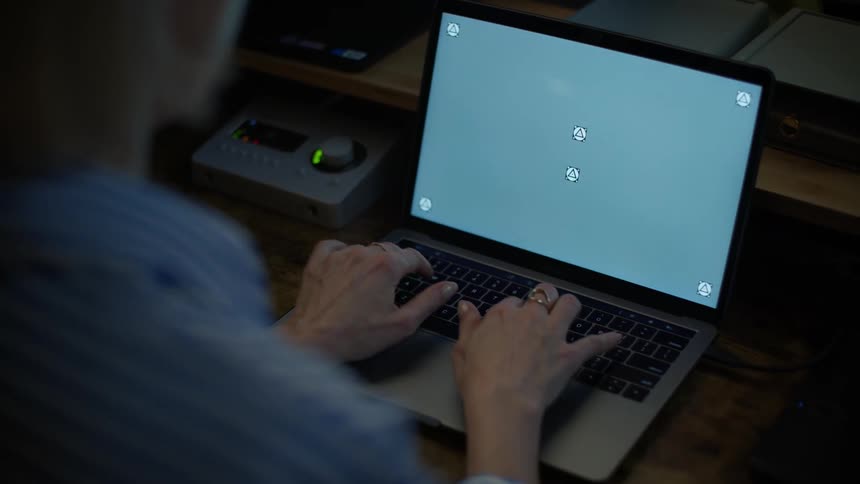 An over-the-shoulder view of a woman's hands typing on a laptop with a screen ready for compositing in a dark room