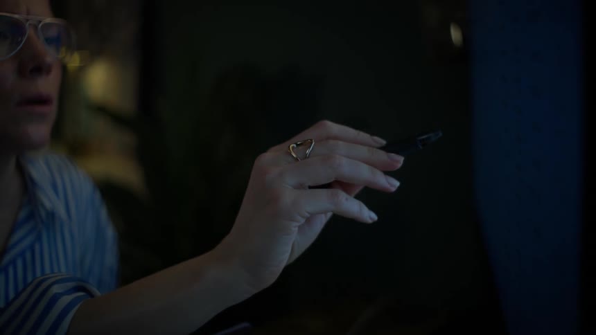A focused female digital artist works late into the night, drawing with a stylus on a tablet in her dimly lit home studio