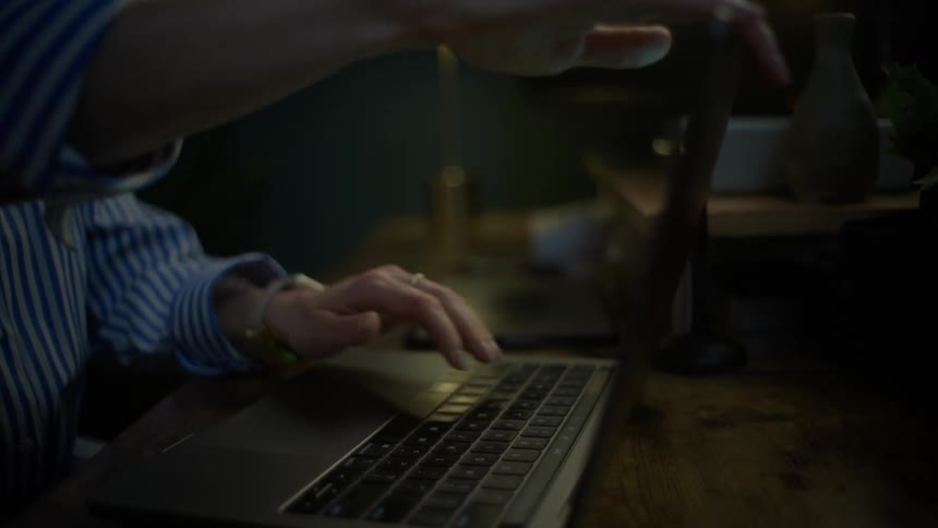 Close up of hands typing on a laptop in a dark room before slowly closing the lid