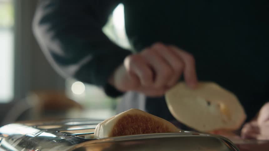 Slow motion close-up of a hand taking freshly toasted bagel halves out of a chrome toaster for breakfast