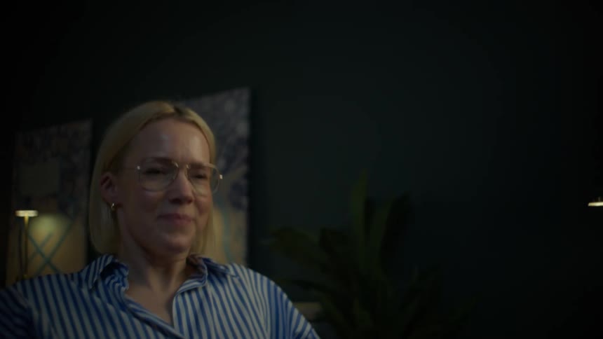 A woman working late at night in a dimly lit room finishes her task, closes her laptop, and smiles with satisfaction