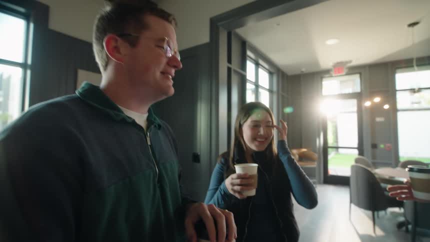 A diverse group of young friends enjoys coffee and conversation in a sunny, modern apartment building lounge