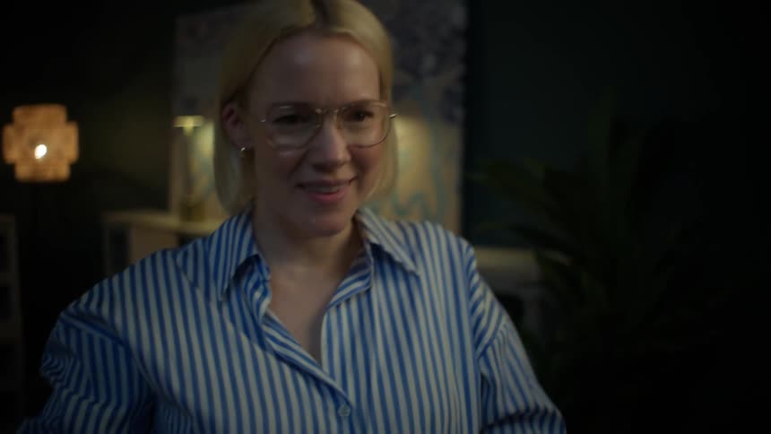 A smiling woman in glasses closes her laptop, satisfied after finishing her work for the night in a dimly lit room