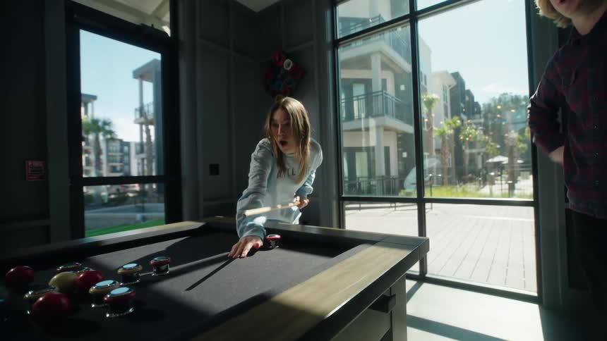 A young woman celebrates with a laugh and a high-five after making a successful shot in a game of bumper pool with her friend in slow motion