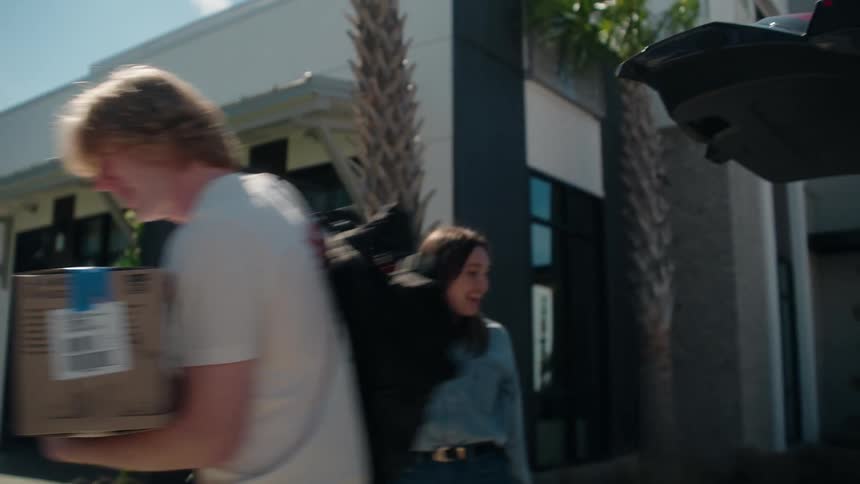 An excited young woman smiles as she pulls her suitcase towards her new modern apartment building on move-in day
