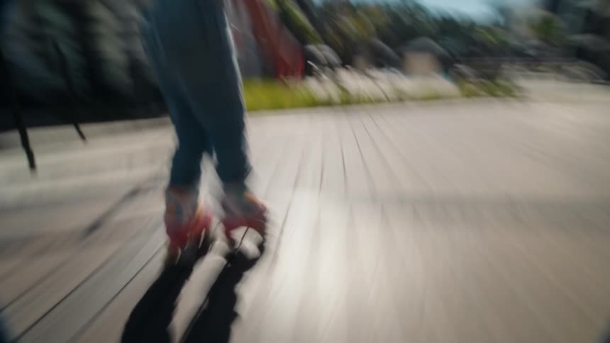 A low-angle tracking shot follows a young girl on colorful roller skates as she glides along a boardwalk on a bright sunny day